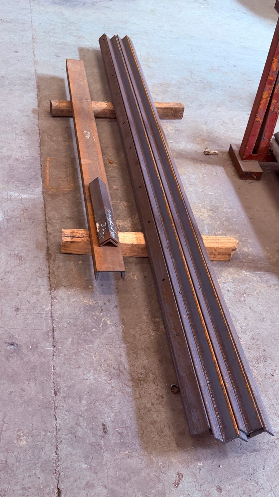Steel angle sections on timber dunnage with hand-chalked piece numbers