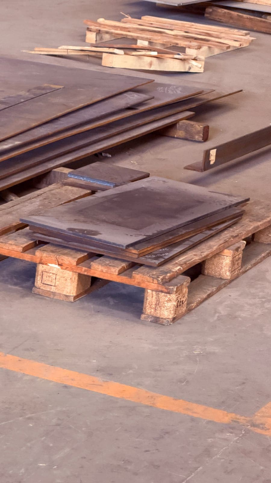 Steel plate off-cuts stacked on a timber pallet on a yard floor
